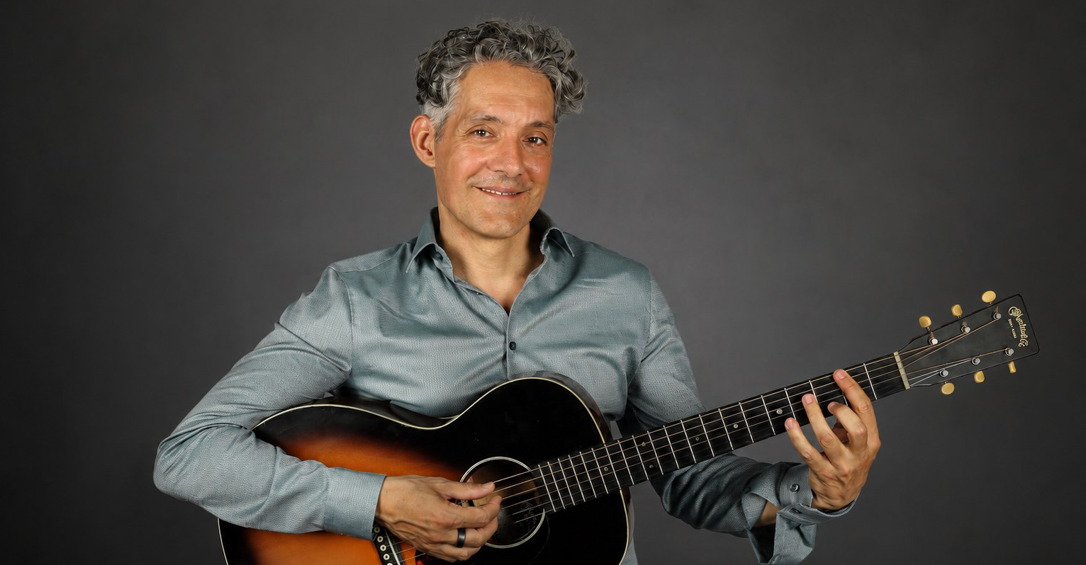 Stephan Bienwald lächelt zurückhaltend mit seiner Gitarre